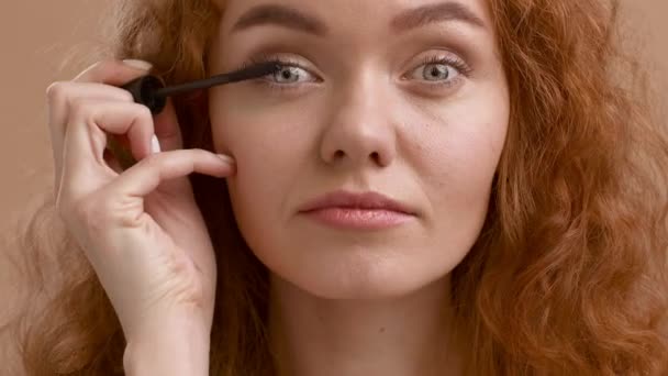 Rödhårig ung dam Tillämpa Mascara på ögonfransar på Beige bakgrund — Stockvideo