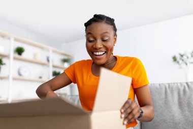 Teslimat, uzaktan alışveriş. Gülümseyen siyah kadın karton paketleri açıyor, evden aldığı parayla mutlu.