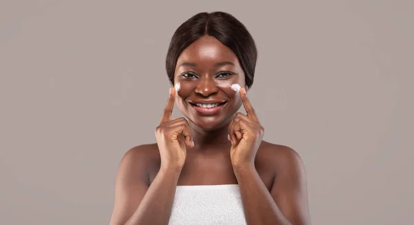 Skönhetsporträtt av glad leende afroamerikansk kvinna Tillämpa ansiktskräm — Stockfoto