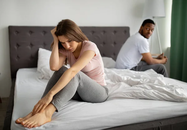Disfuncție erectilă, concept de probleme sexuale. Femeia tânără nefericită stând pe pat, iubitul ei supărat pe fundal — Fotografie, imagine de stoc