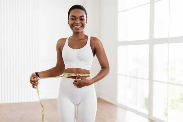 Mulher negra feliz medindo cintura com fita adesiva. Conceito de emagrecimento — Fotografia de Stock