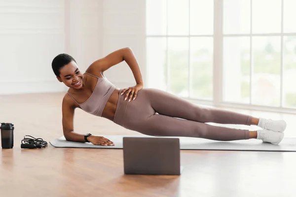 Jovem mulher negra fazendo prancha lateral no tapete com pc — Fotografia de Stock