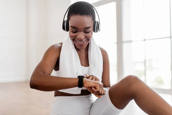 Sporty black lady checking fitness tracker during workout break — Stock Photo, Image
