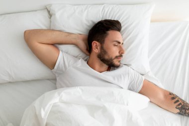 Yorgun milenyum adamı uyuyor, beyaz yatakta uzanıyor, gözleri kapalı dinleniyor, üst manzara, kopyalama alanı