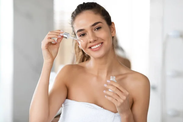 Mujer feliz aplicando suero facial con gotero hidratante en la piel interior — Foto de Stock