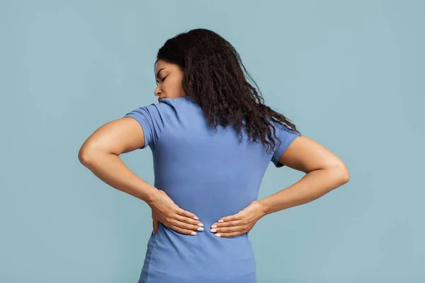 Concepto de dolor de espalda. dama afroamericana tocando hacia atrás, teniendo problemas de columna vertebral, de pie sobre fondo azul —  Fotos de Stock