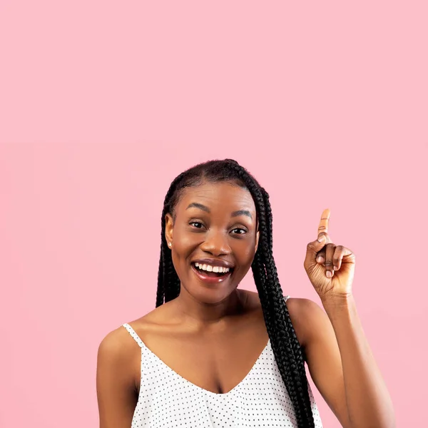 Smiling millennial black woman in white summer dress pointing upwards at empty space on pink studio background — стоковое фото