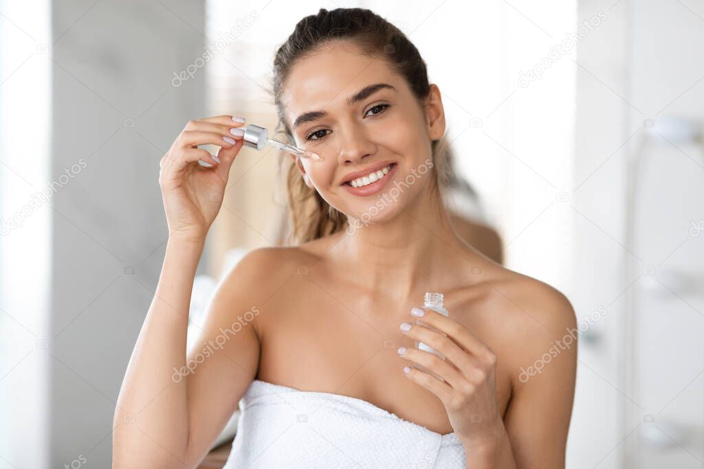 Happy Woman Applying Facial Serum With Dropper Moisturizing Skin Indoor