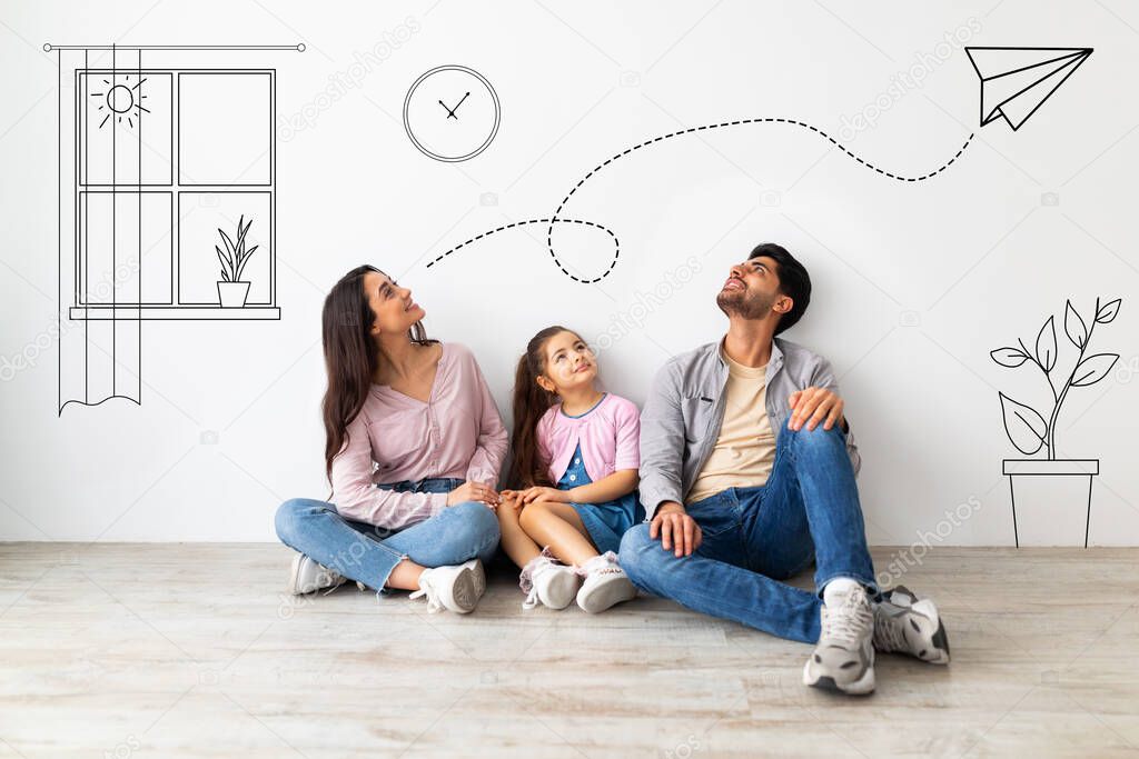 Young family of three imagining interior of their new flat, sitting on floor near white wall with doodle drawings