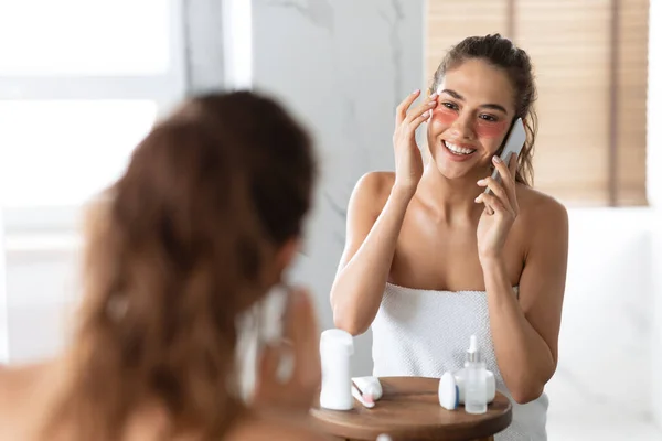 Щаслива жінка розмовляє по телефону Застосовуючи патчі у ванній кімнаті — стокове фото