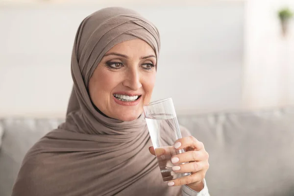Allegra donna matura mediorientale che beve acqua a casa — Foto Stock