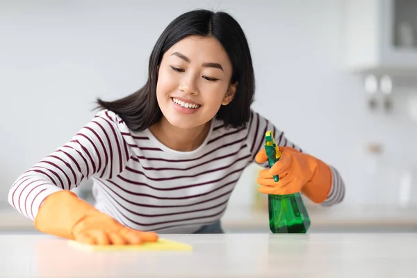 스프레이와 옷감으로 식탁을 청소하는 행복 한 이시아 여자 — 스톡 사진