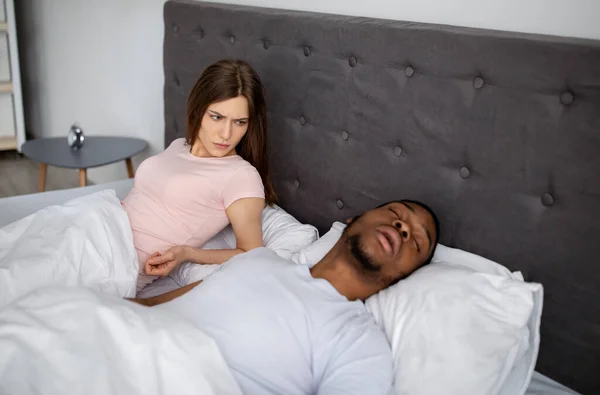 Millennial schwarzer Mann schnarcht und belästigt seine gereizte schlaflose Frau zu Hause im Bett — Stockfoto