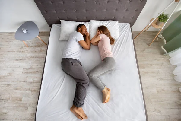 Pełna długość czułej wielorasowej pary sypiającej ze sobą na łóżku, zwróconej ku sobie, widok z góry — Zdjęcie stockowe