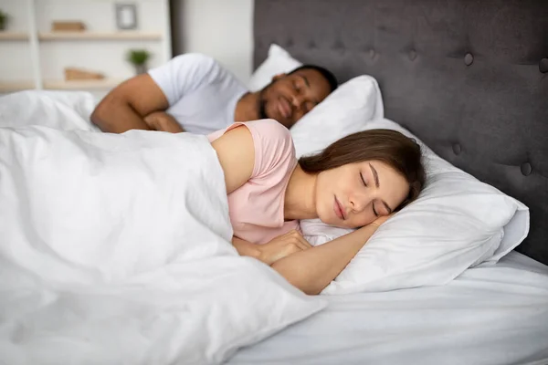 A fiatal kaukázusi nő és a fekete férje együtt fekszenek otthon az ágyban. Szerető kapcsolat — Stock Fotó