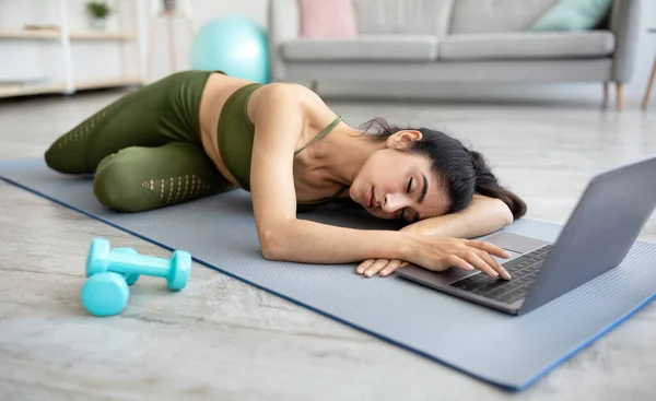 Tired young Indian woman sleeping on yoga mat in front of laptop, too exhausted from online training at home — 스톡 사진