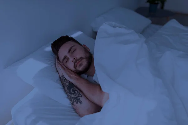 Красивый мужчина видит сладкие сны, мирно отдыхает в своей удобной постели дома, лежа с закрытыми глазами — стоковое фото