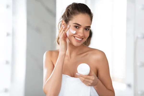 Female Applying Facial Cream Holding Moisturizer Jar Posing In Bathroom — 图库照片