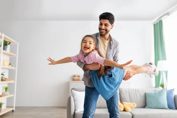 Happy father playing with kid at home, carrying little daughter like plane, holding girl on hands, copy space — 图库照片