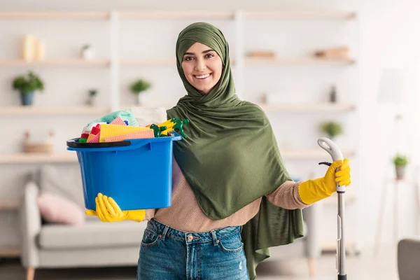 Fröhliche muslimische Hausfrau hält Eimer mit Putzmitteln in der Hand — Stockfoto