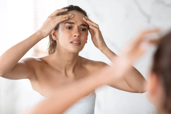 Frustrado señora apretando espinilla en la frente en baño moderno en interiores —  Fotos de Stock