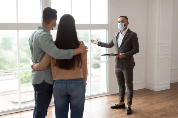 Агент по недвижимости в медицинской маске показывает покупателям новую квартиру — стоковое фото