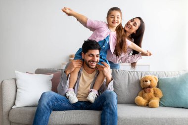 Neşeli genç doğu ebeveynleri çocukla eğleniyor, oynuyor ve gülüyor, evde birlikte vakit geçiriyorlar.