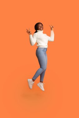 Neşeli siyah kadın havaya atlıyor ve iki eliyle barışı işaret ediyor.