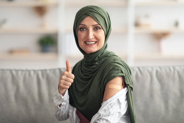 Vaccinato musulmano signora in hijab gesturing pollice-su mostrando braccio indoor — Foto Stock