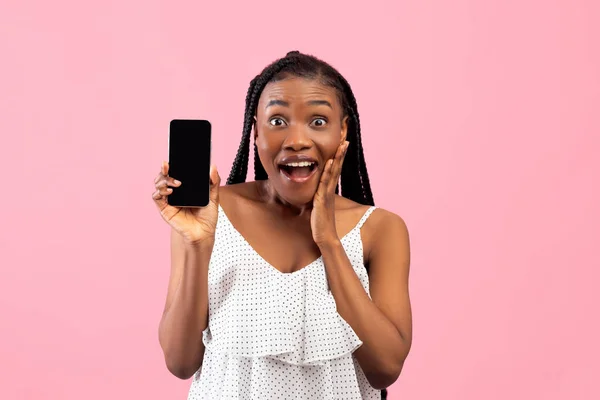 Surprised black woman holding blank smartphone with mockup for mobile app design on pink studio background — 스톡 사진