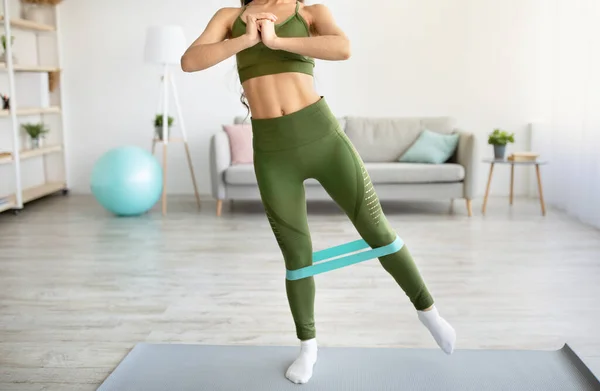 Unrecognizable young lady exercising with elastic band, working out her strength in living room — Stock Photo, Image