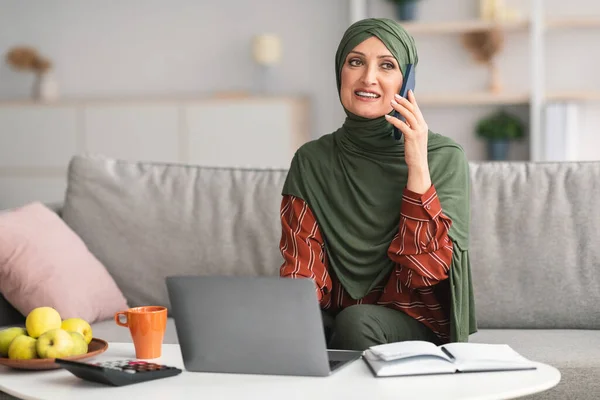 Perempuan Muslim Mature Berbicara Pada Telepon Menggunakan Laptop Di Rumah — Stok Foto