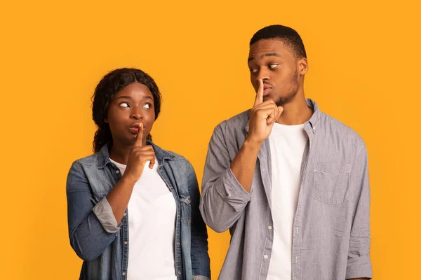 Es un secreto. Pareja negra haciendo señal de silencio, manteniendo los dedos índice en los labios — Foto de Stock