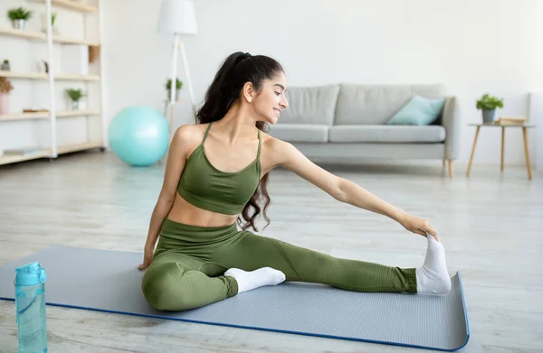 Giovane signora indiana che si estende su tappetino yoga, facendo allenamento domestico, facendo esercizi di flessibilità a casa — Foto Stock