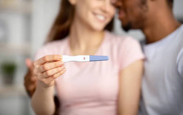 Primo piano di felice giovane coppia multirazziale mostrando test di gravidanza positivi a macchina fotografica, felice di avere un bambino, messa a fuoco selettiva — Foto Stock