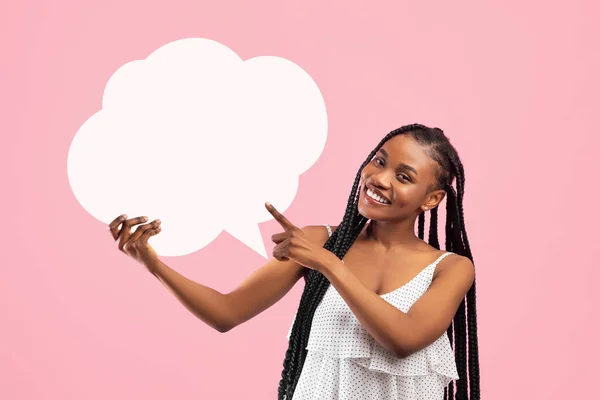 Cheerful black woman with afro bunches pointing at blank speech bubble on pink studio background, mockup for design — 스톡 사진