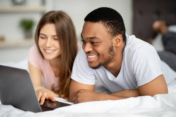 Cariñosa pareja multirracial pasar tiempo juntos en casa, utilizando el ordenador portátil en la cama —  Fotos de Stock