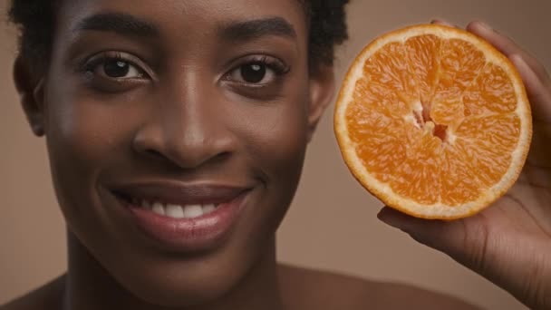 Retrato de mujer africana sosteniendo naranja cerca de la cara, fondo beige — Vídeos de Stock