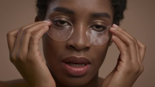 Mujer afroamericana bastante aplicando parches debajo de los ojos sobre fondo beige — Vídeo de stock