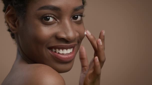 Atractiva dama negra que aplica la crema hidratante de la cara de la piel, fondo beige — Vídeo de stock