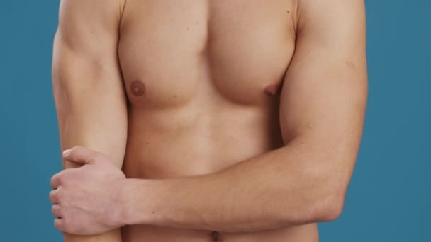 Detailní záběr bez trička svalnatý chlap tření jeho bolestivý loket, trpí trauma nebo zranění, modré pozadí — Stock video