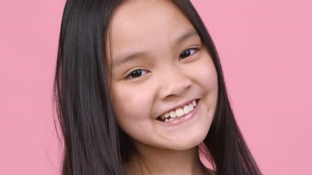 Szczęśliwego dzieciństwa. Adorable szczęśliwy mały azjatycki dziewczyna uśmiecha się szeroko do kamery, pozowanie na różowym tle studio — Wideo stockowe