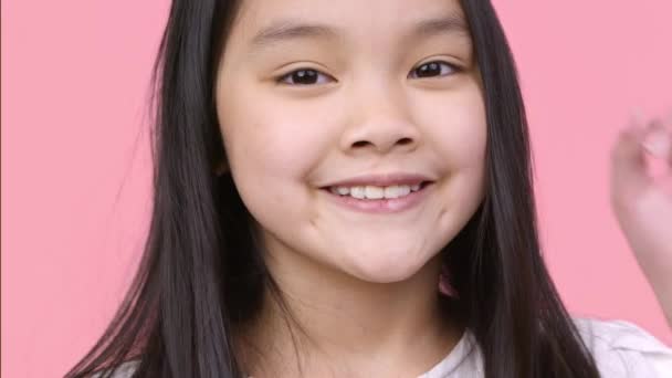 Çocuklar onaylıyor. Küçük sevimli Asyalı kız kameraya jest yapıyor ve gülümsüyor, mutlu, pembe stüdyo geçmişi var. — Stok video
