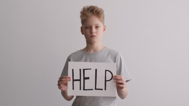 Жертва знущань. Портрет засмученого хлопчика-підлітка, який тримає плакат зі словом HELP, на жаль, дивиться на камеру , — стокове відео