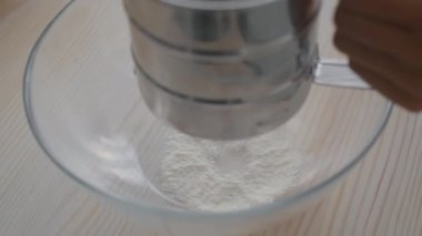 Pasta tarifi. Fırıncı klozette paslanmaz elek ile un yudumluyor, hamur için malzeme ekliyor, mutfakta yemek pişiriyor.