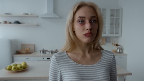 Close up portrait of young battered woman with wounds and bruises on face standing alone at kitchen, slow motion — Stockvideo