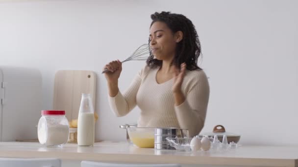 Cooking is fun. Young emotional african american woman singing with whisk and dancing, enjoying music at kitchen alone — Stockvideo