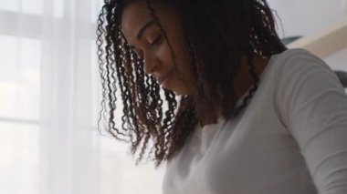 Odaklanmış Afro-Amerikan kadın portresinin hemen altında evde bir şeyler yapıyor, hamur yoğuruyor ya da çamaşır yıkıyor.