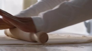 Profesyonel kadın fırıncı hamuru ahşap broşla yuvarlıyor ve ona dokunuyor, mutfakta işyerinde hamur işi hazırlıyor.