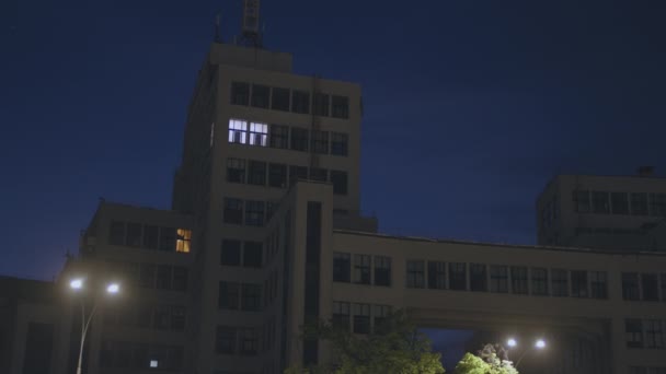 Vida nocturna e conceito de excesso de trabalho. Edifício de escritório vazio grande com duas janelas iluminando na escuridão, espaço vazio — Vídeo de Stock